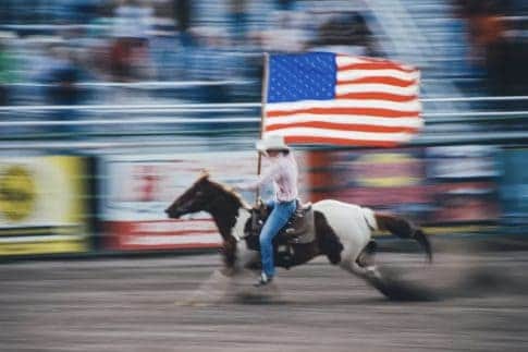 At a rodeo, a horseback rider rides while he flies an American flag