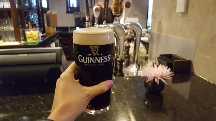 A woman with painted nails holds up a Guiness beer in a bar's kitchen