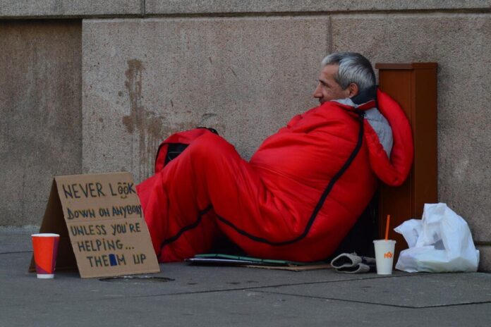 A man with a sign sleeping outside struggling with homelessness