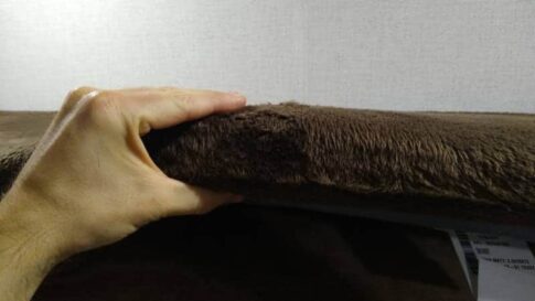 A hand squishing a thin 3-inch thick upholstered kids mattress.