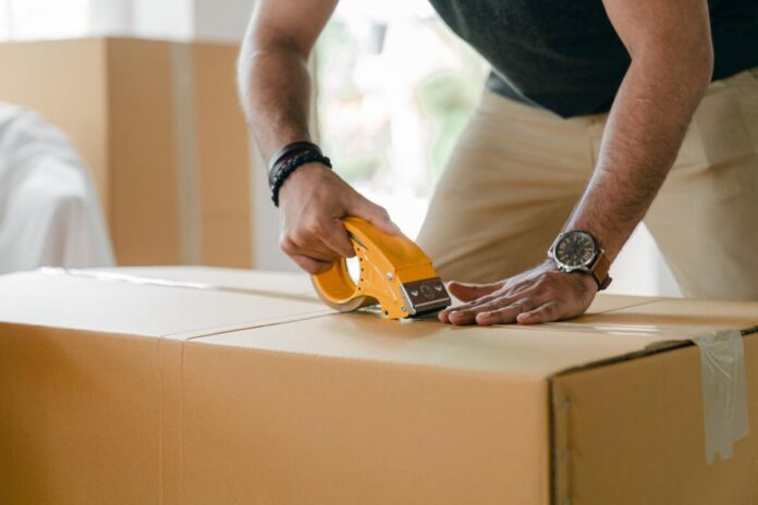 A man tapes up a cardboard box when he has his RV packing list all finished