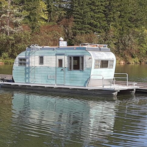 A vintage trailer houseboat floats on a lake