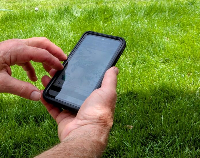 Man's hands holding cell phone; grass background Gail Marsh image (no attribution needed)